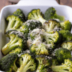 Roasted broccoli with parmesan cheese in a white ceramic baking dish on a rustic wooden table