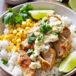 Sliced grilled chicken breast over white rice with roasted corn, elote-style sauce, lime, and cilantro in a bowl on a wood table