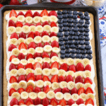 American Flag Fruit Pizza decorated with fresh strawberries, bananas, and blueberries on a sugar cookie crust for a festive 4th of July treat.
