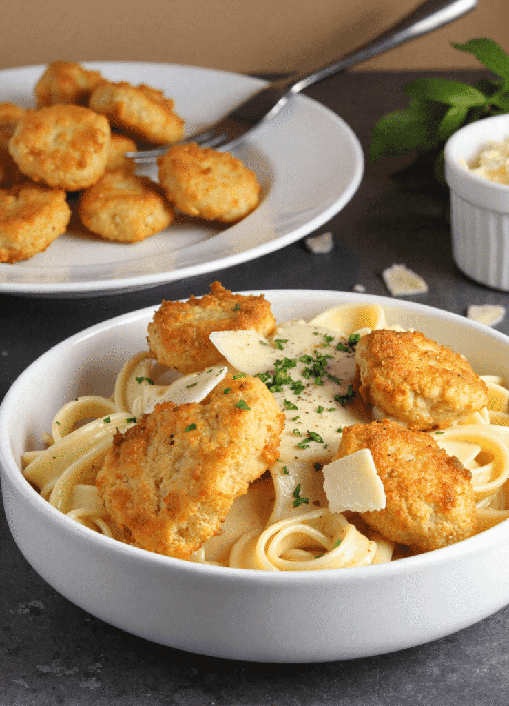 Bowl of garlic butter chicken bites with creamy parmesan pasta garnished with parsley and parmesan shavings.