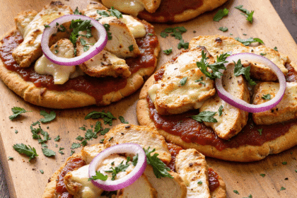 grilled BBQ chicken flatbreads with barbecue sauce, grilled chicken breast slices, melted cheese, red onion, and fresh herbs on wooden serving board