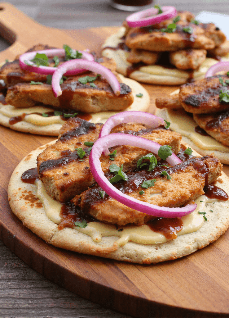 grilled chicken flatbread pizza topped with barbecue sauce, grilled chicken, melted cheese, and sliced red onions, served on a wooden board