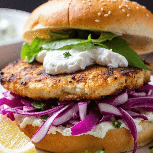 Close-up of a grilled fish sandwich layered with crispy red cabbage slaw, fresh spinach, and creamy tzatziki on a sesame bun.