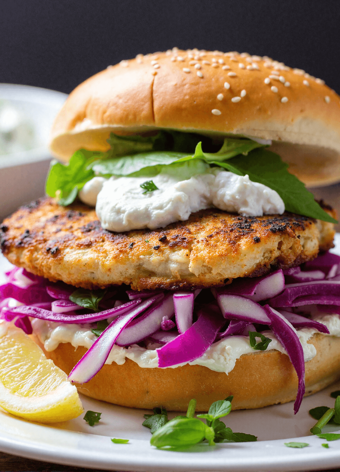 Close-up of a grilled fish sandwich layered with crispy red cabbage slaw, fresh spinach, and creamy tzatziki on a sesame bun.
