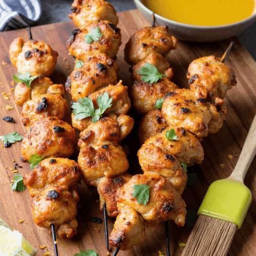 Grilled honey lime chicken skewers served on a wooden board with fresh lime wedges and cilantro
