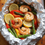 Garlic butter shrimp foil packets with lemon slices, bell peppers, and asparagus, ready to be grilled in foil.