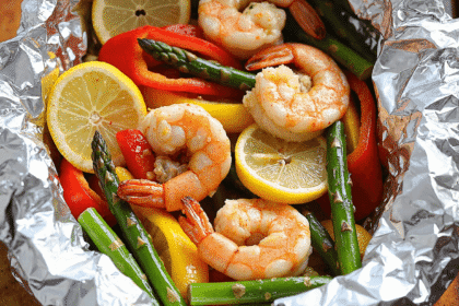 Garlic butter shrimp foil packets with lemon slices, bell peppers, and asparagus, ready to be grilled in foil.