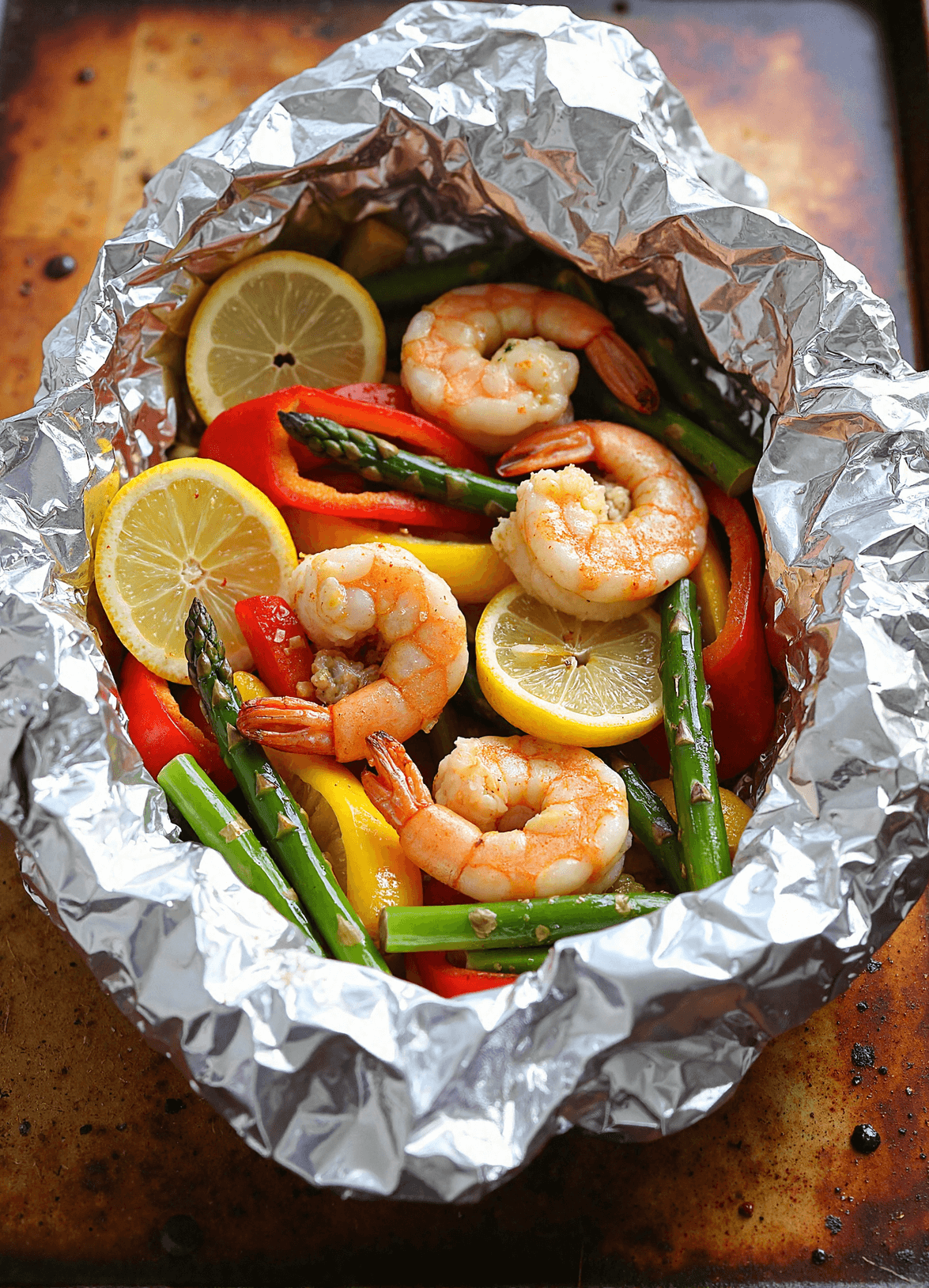 Garlic butter shrimp foil packets with lemon slices, bell peppers, and asparagus, ready to be grilled in foil.
