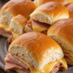 Close-up of ham and cheese Hawaiian roll sliders with melted American cheese on sweet golden buns.