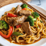 Healthy Mongolian beef noodles in sauce with broccoli, red peppers, and sesame seeds.