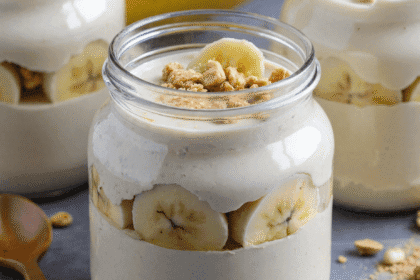 Creamy high protein banana pudding in glass jars layered with banana slices and granola, served on a gray stone background