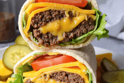 Close-up of a high protein cheeseburger wrap with melted cheddar, ground beef, lettuce, and tomato stacked on a plate with pickles.