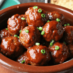 Slow-cooked honey BBQ meatballs in a brown crockpot glazed with thick barbecue sauce and topped with sliced green onions.