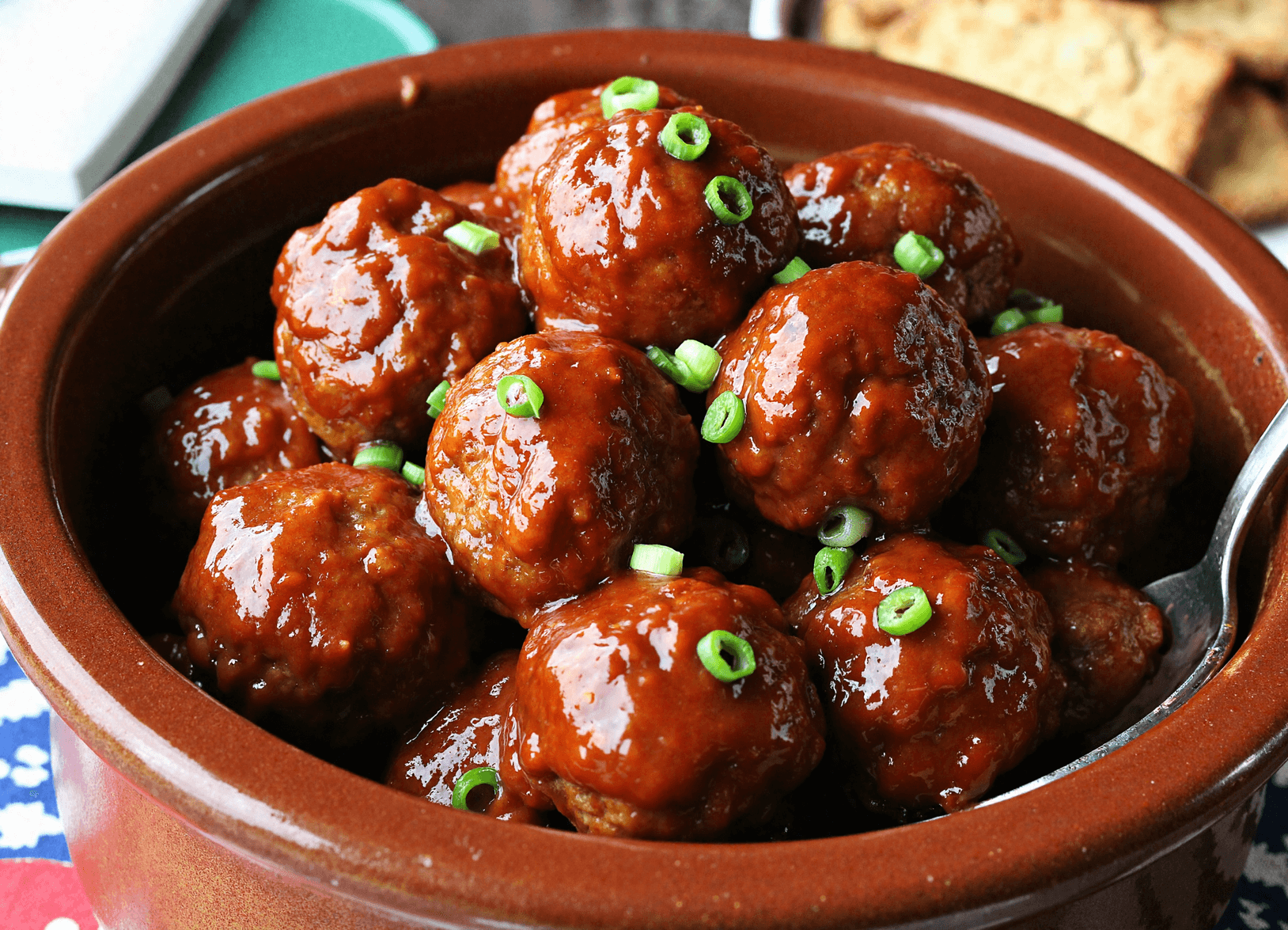 Slow-cooked honey BBQ meatballs in a brown crockpot glazed with thick barbecue sauce and topped with sliced green onions.