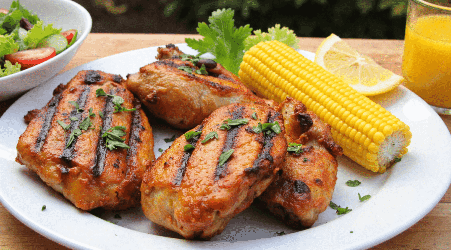 grilled honey chicken thighs on a plate with corn on the cob, lemon wedge, and summer salad