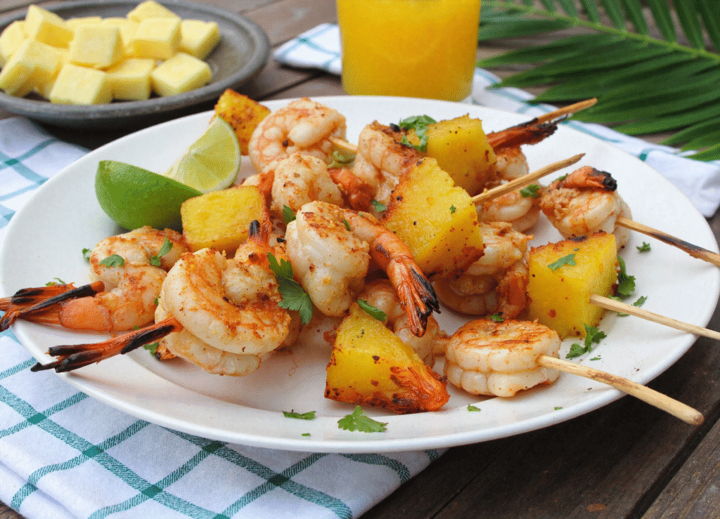 Honey lime shrimp and pineapple skewers on a white plate, served with fresh lime wedges and tropical juice, perfect for summer grilling.
