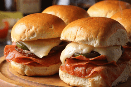 Hot Italian sub sliders with melted provolone, deli pepperoni, and pickles on toasted slider buns served on a wooden board with steam rising.