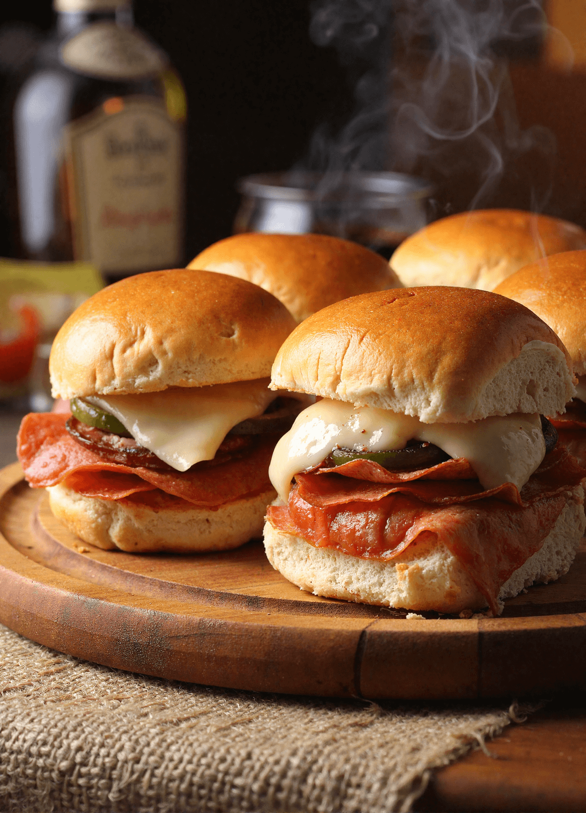 Hot Italian sub sliders with melted provolone, deli pepperoni, and pickles on toasted slider buns served on a wooden board with steam rising.