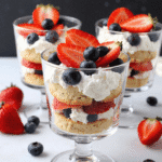 Mini berry trifles with strawberries, blueberries, whipped cream, and cake rounds served in small glass dessert cups.
