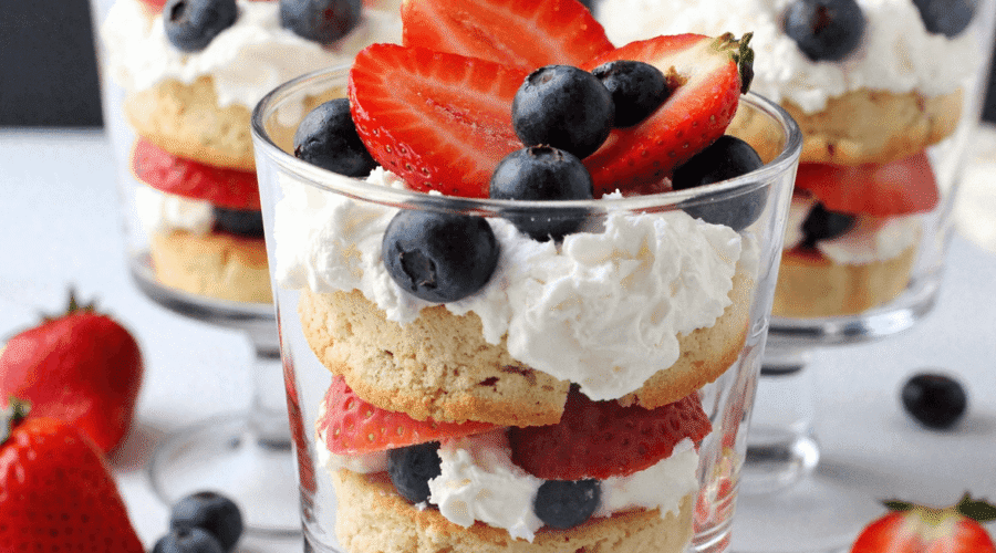 Mini berry trifles with strawberries, blueberries, whipped cream, and cake rounds served in small glass dessert cups.
