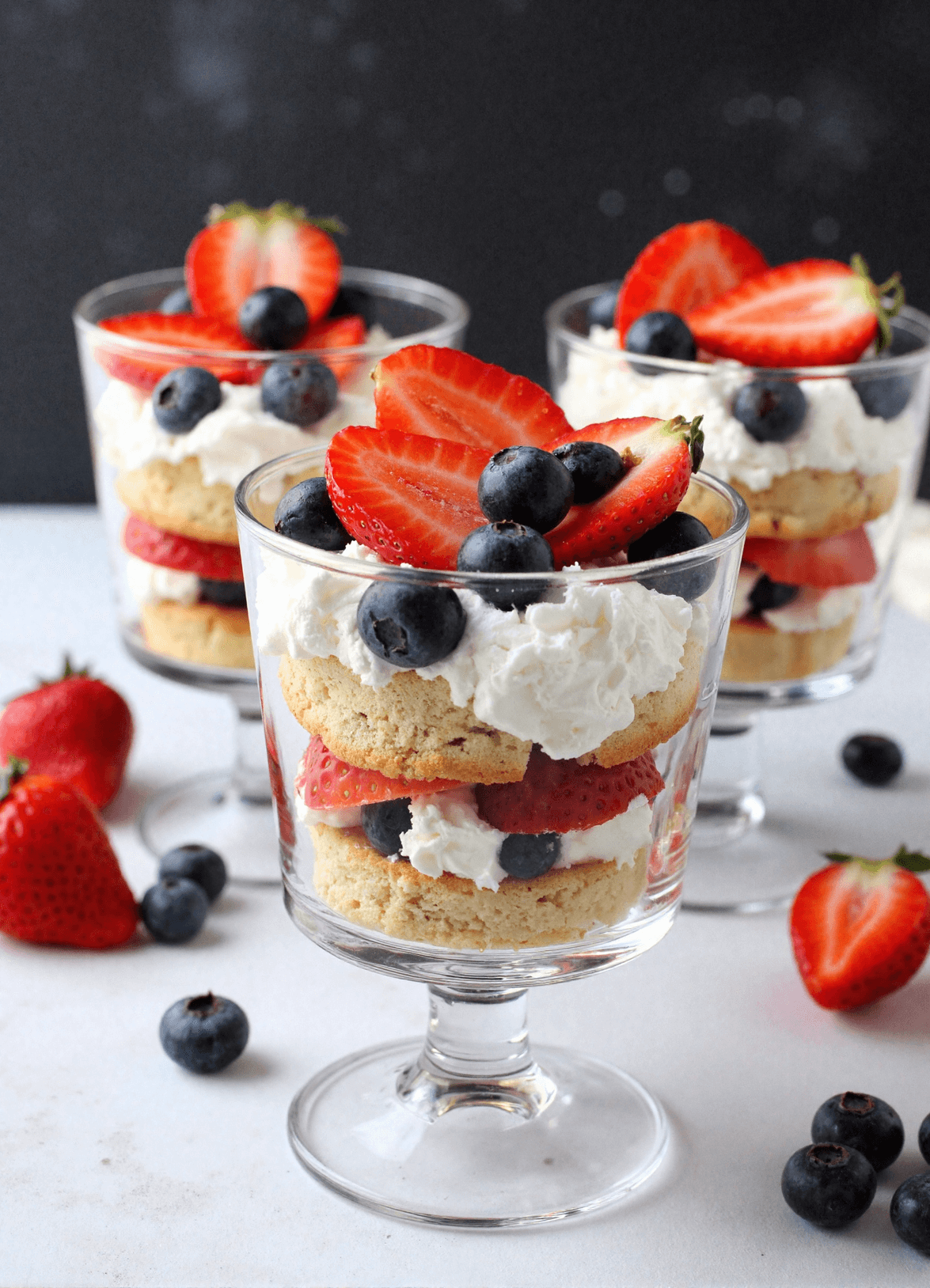 Mini berry trifles with strawberries, blueberries, whipped cream, and cake rounds served in small glass dessert cups.