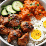 Grilled Korean BBQ chicken leg and thigh with jasmine rice, sliced cucumbers, carrots, kimchi-style mash, and soft-boiled egg.