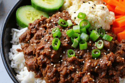 Korean ground beef bowl with rice, sliced cucumbers, pickled carrots, and cauliflower rice, topped with sesame seeds and green onions.