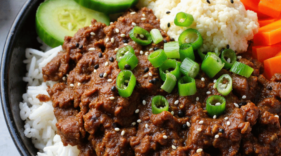 Korean ground beef bowl with rice, sliced cucumbers, pickled carrots, and cauliflower rice, topped with sesame seeds and green onions.
