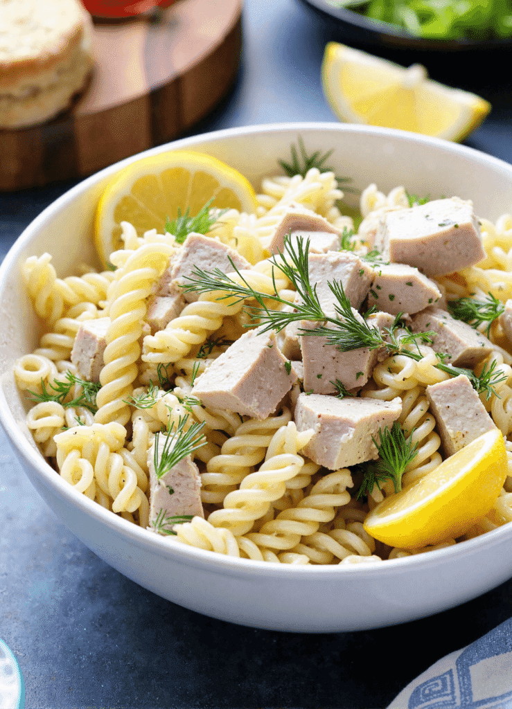 Close-up of lemon dill tuna pasta salad in a gray bowl with penne pasta, creamy tuna, fresh dill, and lemon slices. A heart-healthy, make-ahead tuna pasta salad.
