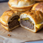 Mini round cheeseburger pocket sliced in half showing juicy ground beef patty, melted cheese, and sliced pickles inside a soft golden crust.
