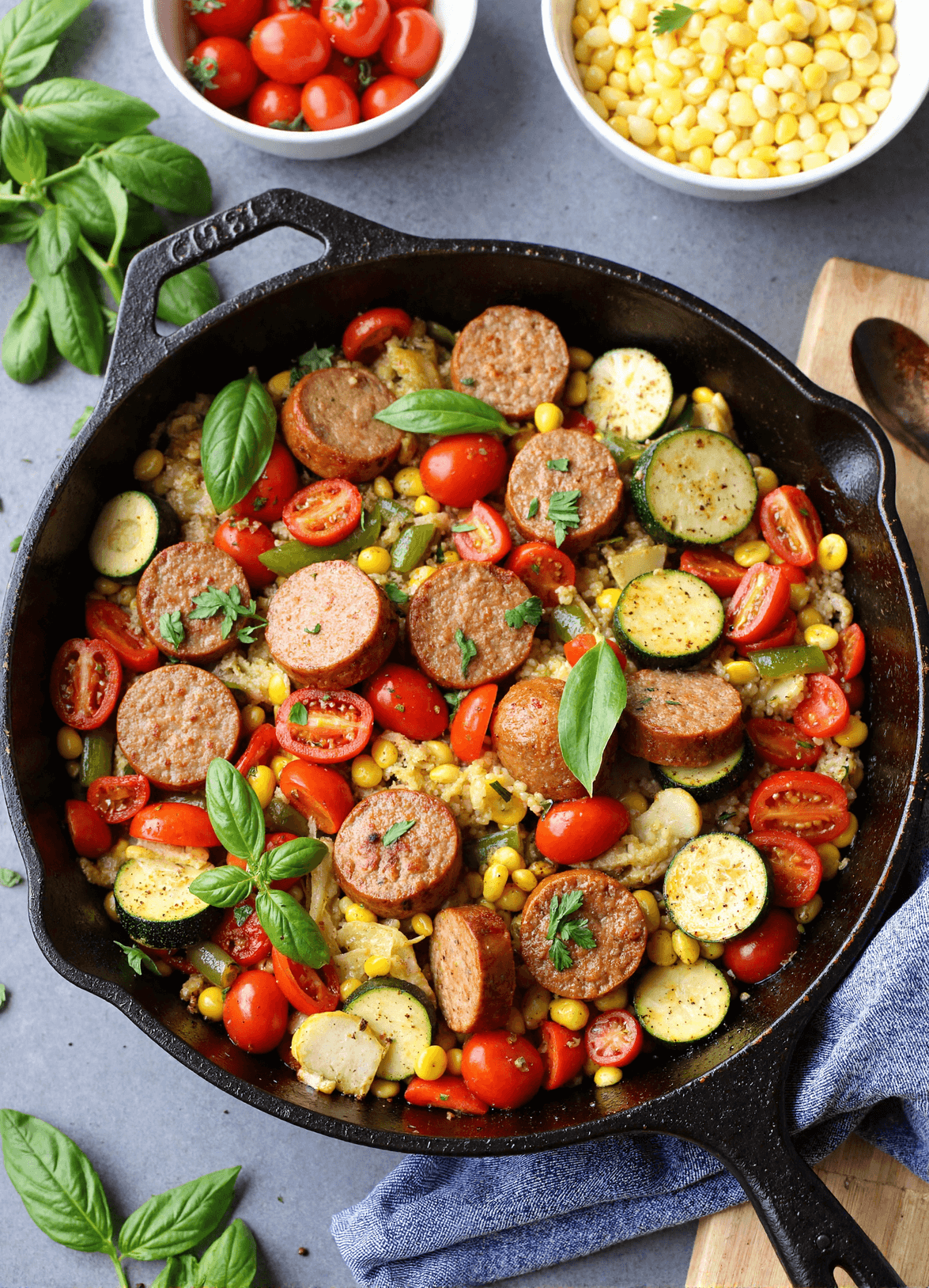 one-pan summer veggie chicken sausage skillet with zucchini, bell peppers, cherry tomatoes, corn, and basil in a cast iron skillet