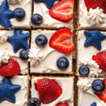 Top view of sliced red, white, and blue cheesecake bars topped with fresh strawberries and blueberries on a graham cracker crust.