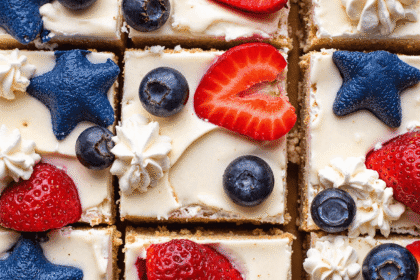 Top view of sliced red, white, and blue cheesecake bars topped with fresh strawberries and blueberries on a graham cracker crust.