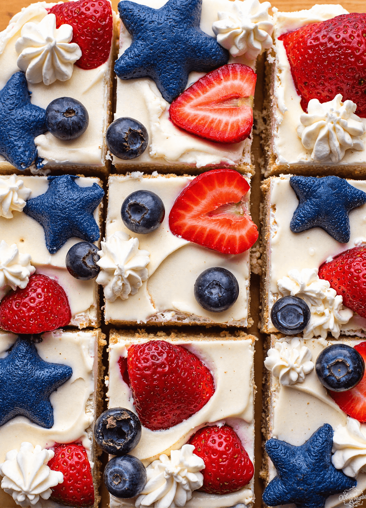 Top view of sliced red, white, and blue cheesecake bars topped with fresh strawberries and blueberries on a graham cracker crust.