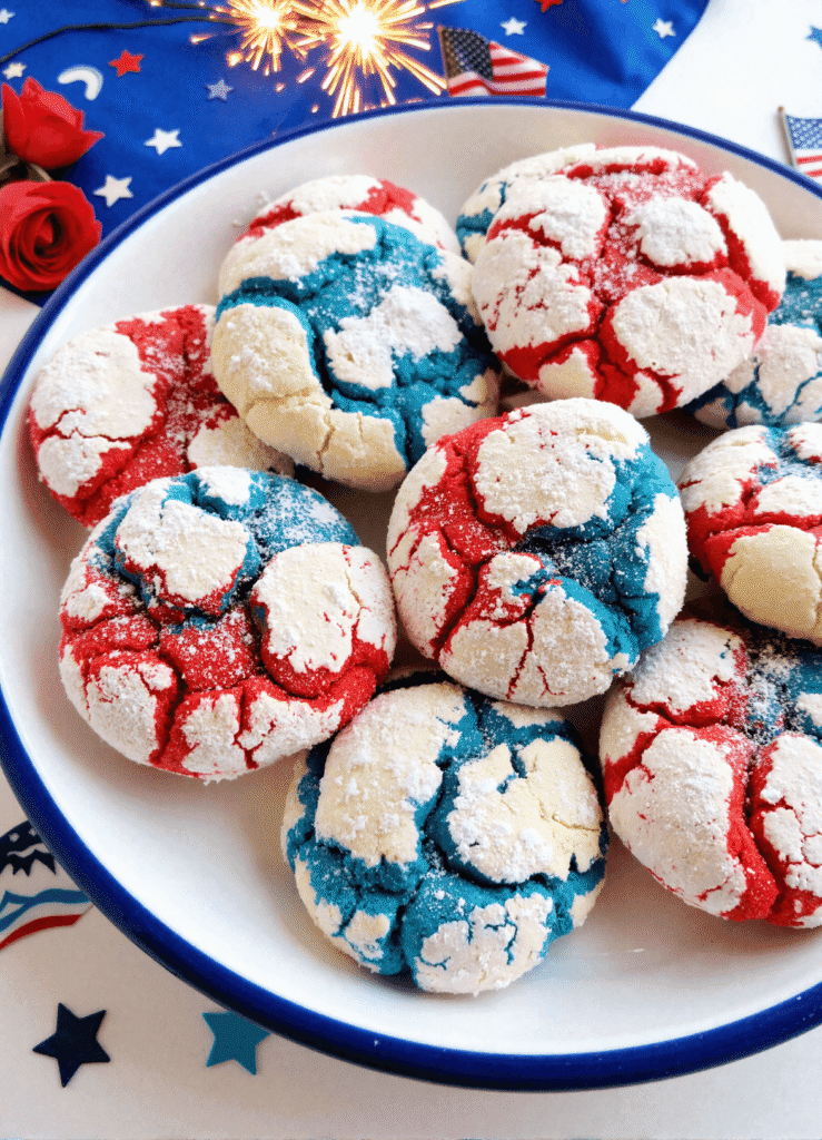 Red, white, and blue crinkle cookies arranged on a round white plate with festive 4th of July decorations.