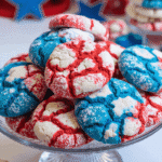 Red white and blue patriotic crinkle cookies stacked on a glass cake stand, dusted with powdered sugar for 4th of July celebrations.