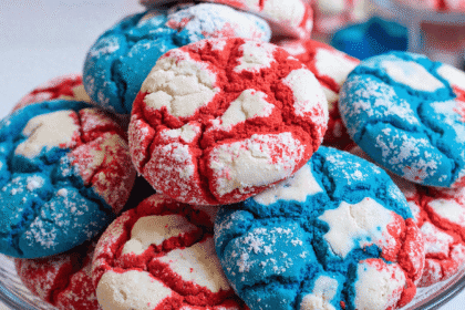 Red white and blue patriotic crinkle cookies stacked on a glass cake stand, dusted with powdered sugar for 4th of July celebrations.
