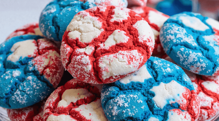 Red white and blue patriotic crinkle cookies stacked on a glass cake stand, dusted with powdered sugar for 4th of July celebrations.