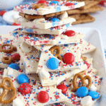 Stacked pieces of red white and blue pretzel bark made with white chocolate, patriotic sprinkles, mini pretzels, and M&Ms on a marble tray.