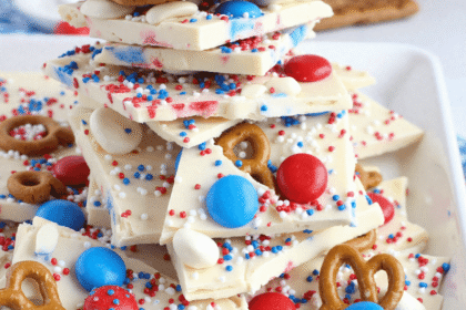 Stacked pieces of red white and blue pretzel bark made with white chocolate, patriotic sprinkles, mini pretzels, and M&Ms on a marble tray.