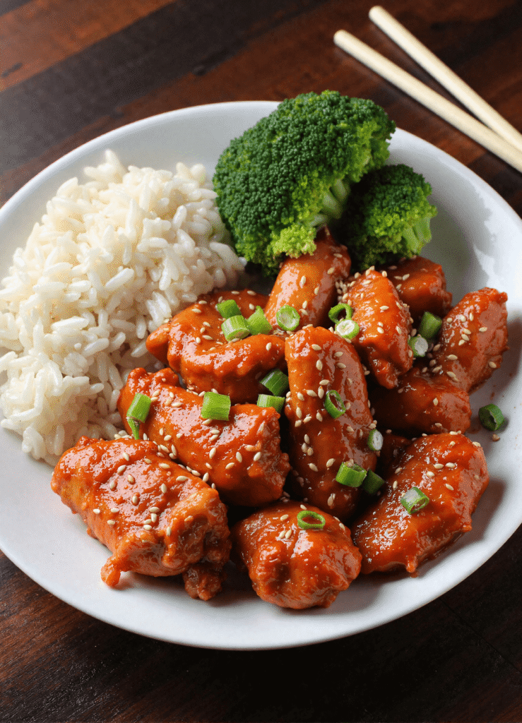 Sticky sweet chili chicken served with jasmine rice and broccoli, garnished with sesame seeds and scallions