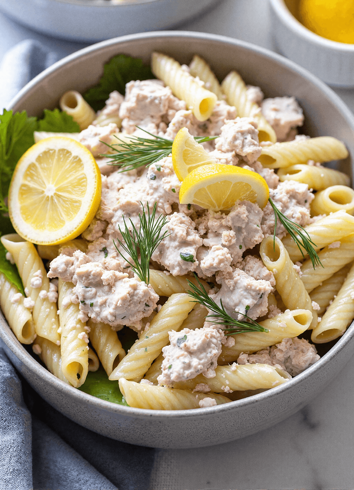 Bowl of tuna pasta salad with lemon and dill featuring rotini pasta, tuna chunks, fresh dill sprigs, and lemon wedges. High-protein pasta salad perfect for picnics.