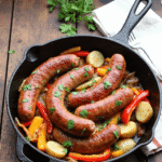 Whole kielbasa sausages roasted with potatoes and peppers in a black skillet