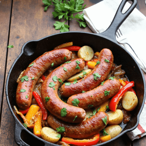 Whole kielbasa sausages roasted with potatoes and peppers in a black skillet