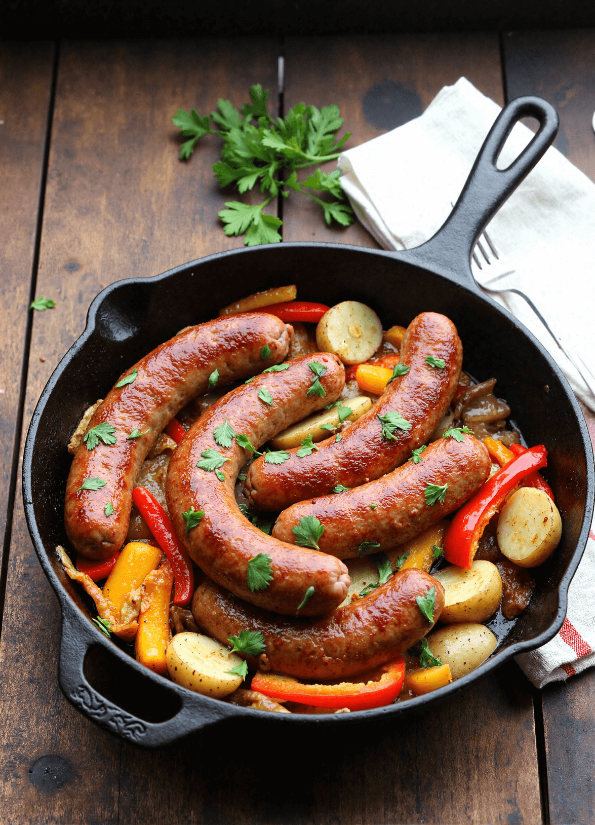 Whole kielbasa sausages roasted with potatoes and peppers in a black skillet