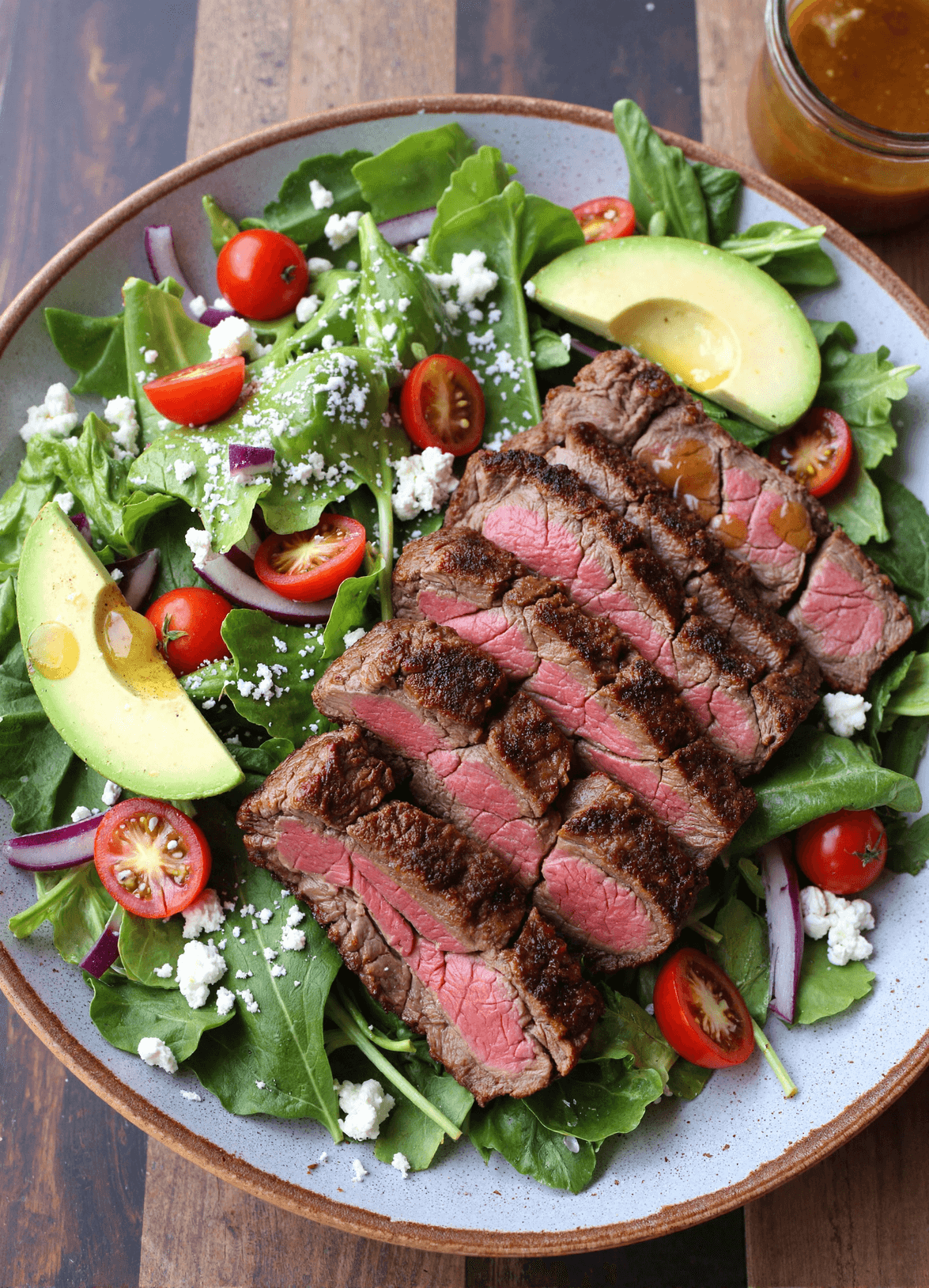 grilled steak salad with avocado, cherry tomatoes, feta cheese, and baby greens on a ceramic plate