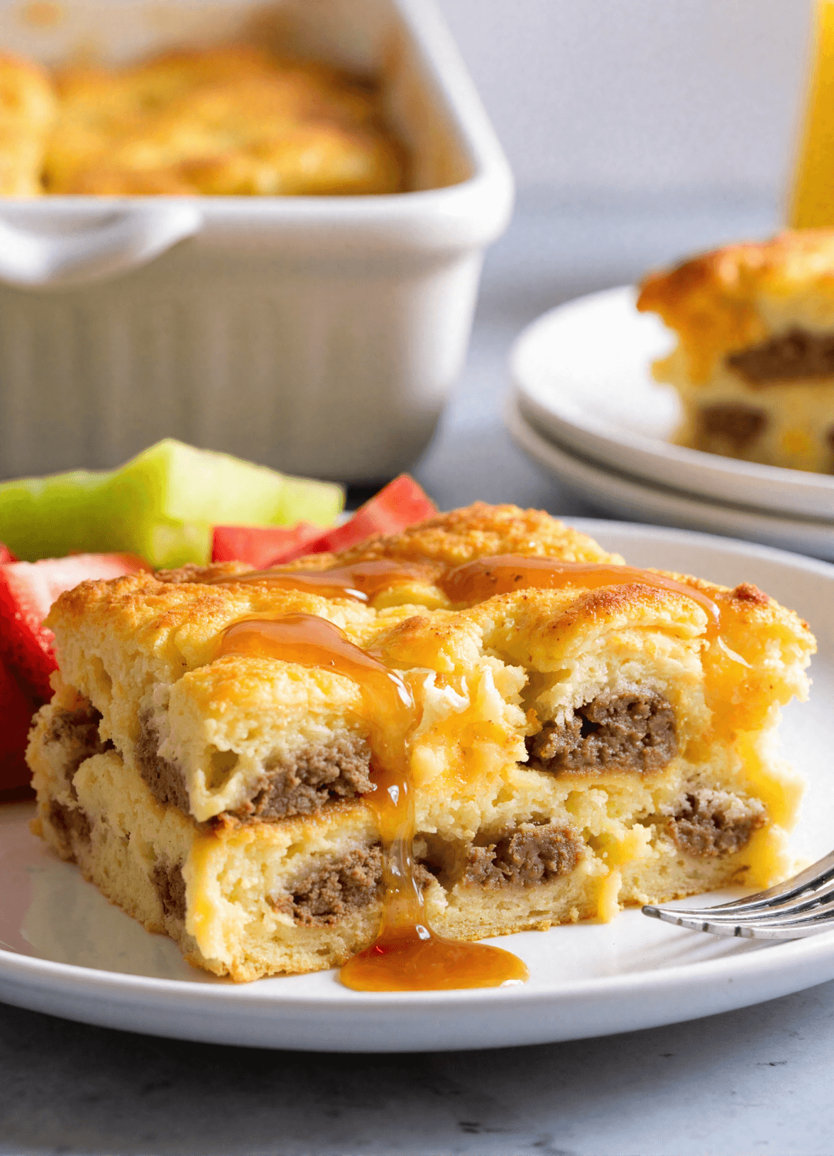 Golden-baked pancake sausage casserole slice on a white plate, drizzled with maple syrup and layered with savory ground sausage and fluffy custard.