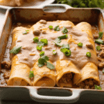Golden breakfast enchiladas topped with creamy sausage gravy and fresh herbs in a ceramic baking dish