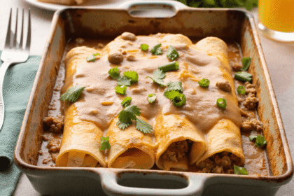 Golden breakfast enchiladas topped with creamy sausage gravy and fresh herbs in a ceramic baking dish