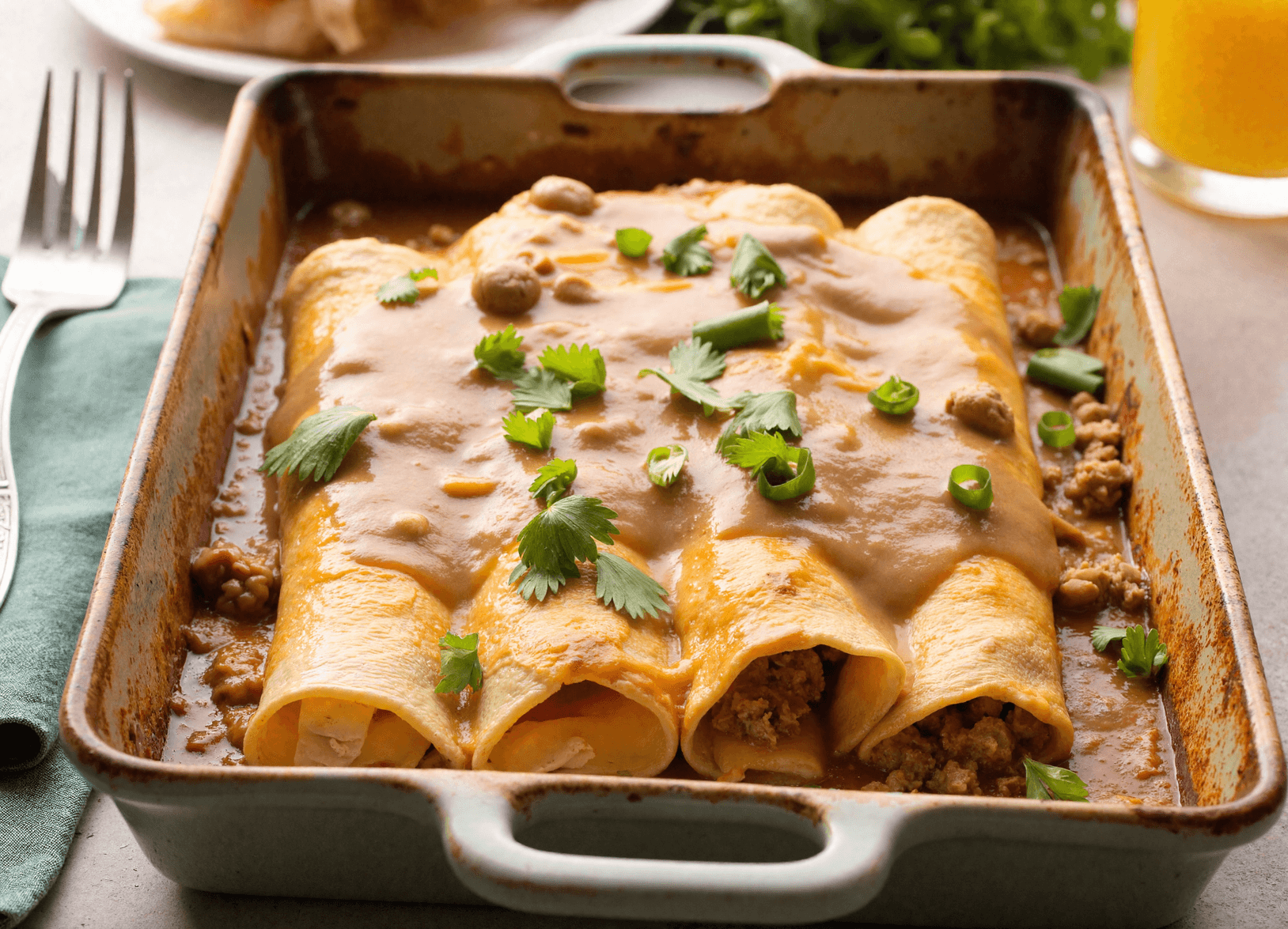 Golden breakfast enchiladas topped with creamy sausage gravy and fresh herbs in a ceramic baking dish